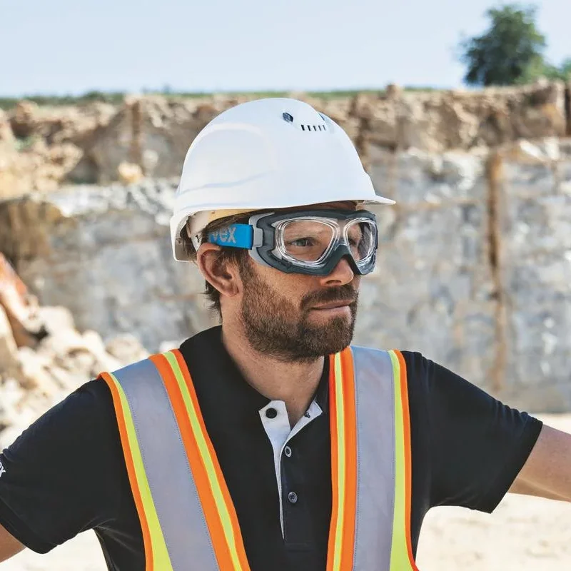 Ein Bauarbeiter mit Schutzhelm und Schutzbrille steht selbstbewusst mit verschränkten Armen vor einer felsigen Ausgrabungsstätte.